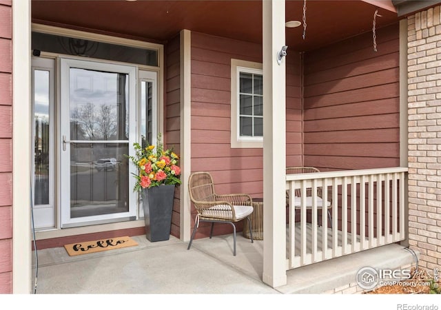 doorway to property featuring a porch and brick siding