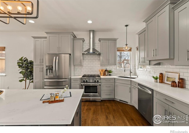 kitchen with a sink, wall chimney range hood, gray cabinetry, stainless steel appliances, and dark wood-type flooring