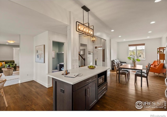 kitchen featuring dark brown cabinetry, dark wood-style flooring, light countertops, open floor plan, and decorative light fixtures