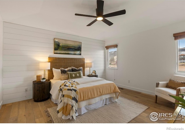bedroom featuring wood walls, baseboards, hardwood / wood-style flooring, and a ceiling fan