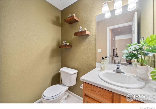 half bath with toilet, vanity, a textured wall, and baseboards