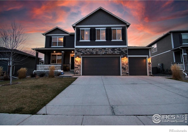 view of front of home featuring concrete driveway, stone siding, a front lawn, a porch, and a garage