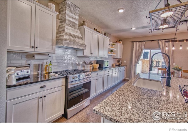 kitchen featuring a sink, white cabinetry, wood finished floors, premium range hood, and gas range