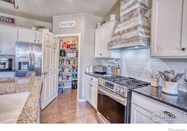 kitchen featuring light wood-type flooring, stainless steel appliances, custom range hood, white cabinets, and decorative backsplash