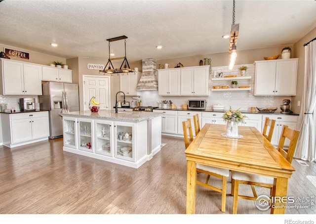 kitchen featuring premium range hood, stainless steel appliances, hanging light fixtures, a sink, and light wood finished floors