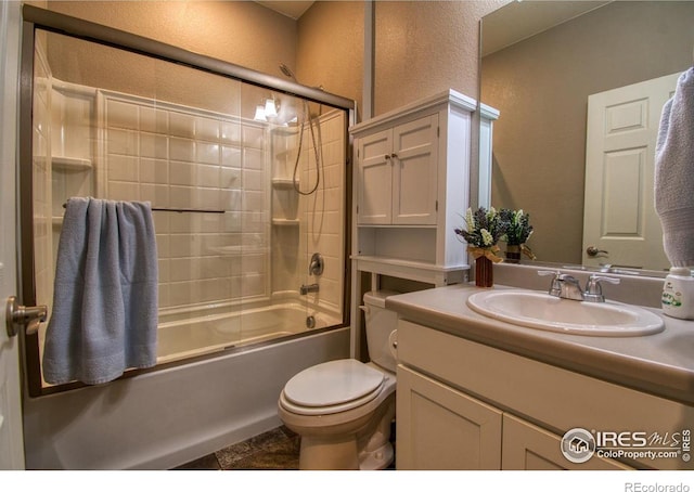 bathroom with combined bath / shower with glass door, toilet, vanity, and a textured wall