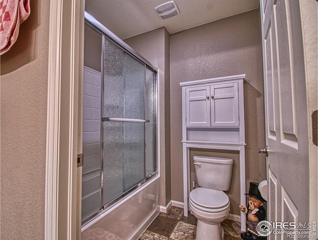 full bath featuring visible vents, stone finish floor, bath / shower combo with glass door, baseboards, and toilet