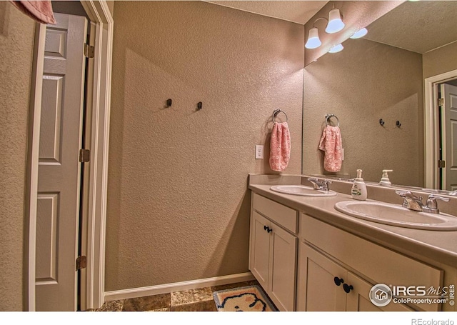 full bath with double vanity, a sink, a textured wall, and baseboards