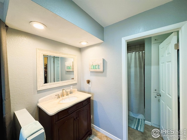 full bath featuring baseboards, a textured wall, and vanity