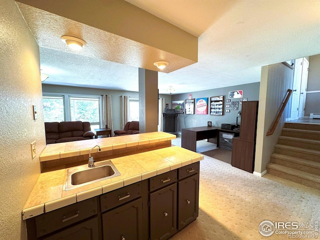 kitchen with a textured ceiling, a peninsula, dark brown cabinets, a sink, and open floor plan