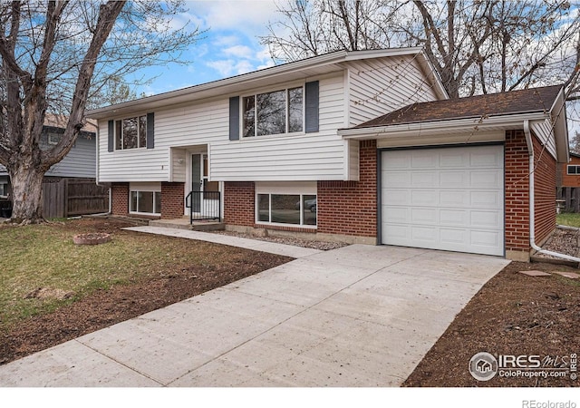 bi-level home featuring driveway, brick siding, a garage, and fence