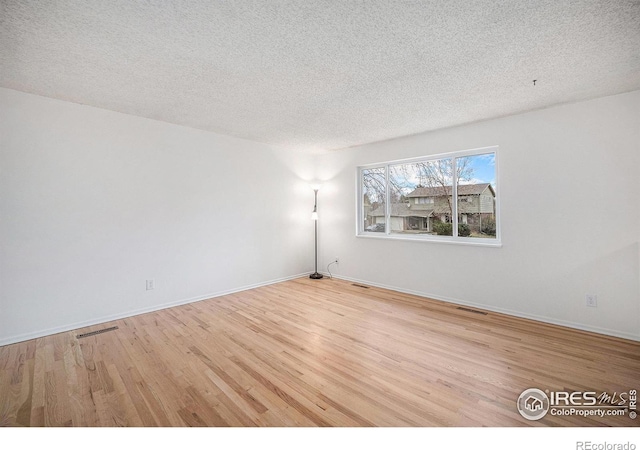 unfurnished room with baseboards, visible vents, wood finished floors, and a textured ceiling