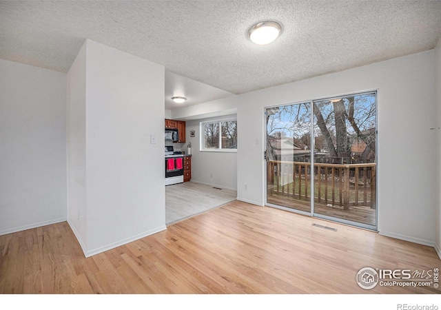 empty room with baseboards, light wood-type flooring, visible vents, and a textured ceiling