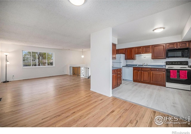 kitchen featuring light wood-style flooring, white appliances, a sink, open floor plan, and brown cabinetry
