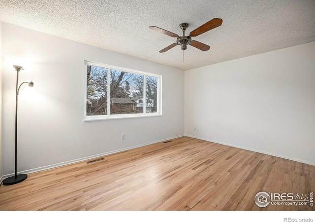 empty room featuring a textured ceiling, visible vents, wood finished floors, and a ceiling fan