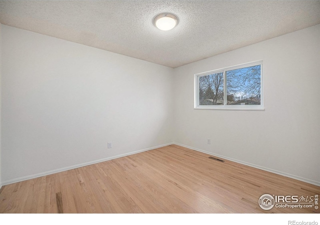 spare room featuring baseboards, visible vents, wood finished floors, and a textured ceiling