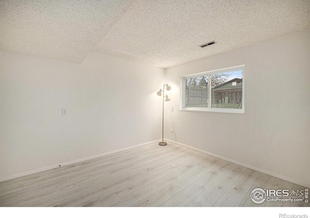 spare room featuring baseboards, a textured ceiling, visible vents, and wood finished floors