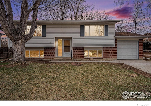 raised ranch featuring a lawn, brick siding, and concrete driveway