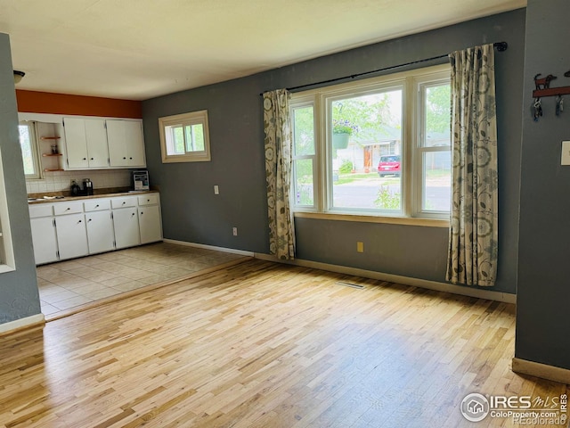117 Welch Ave, Berthoud, CO 80513 - kitchen with open shelves, light wood-style floors, white cabinets, decorative backsplash, and baseboards