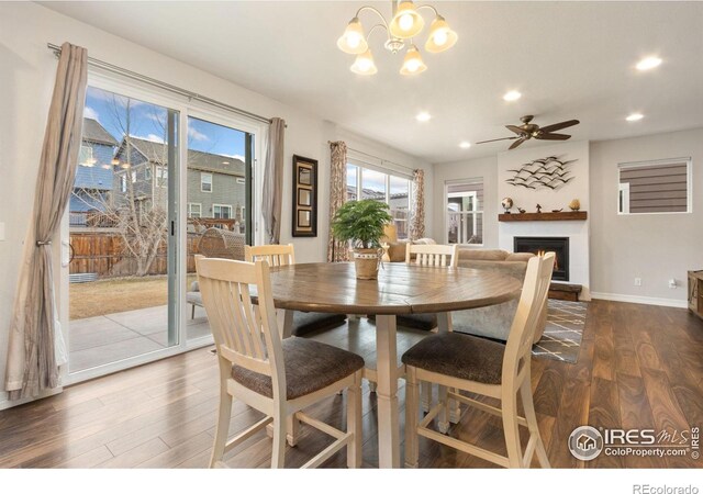 dining space with ceiling fan with notable chandelier, a lit fireplace, wood finished floors, and recessed lighting