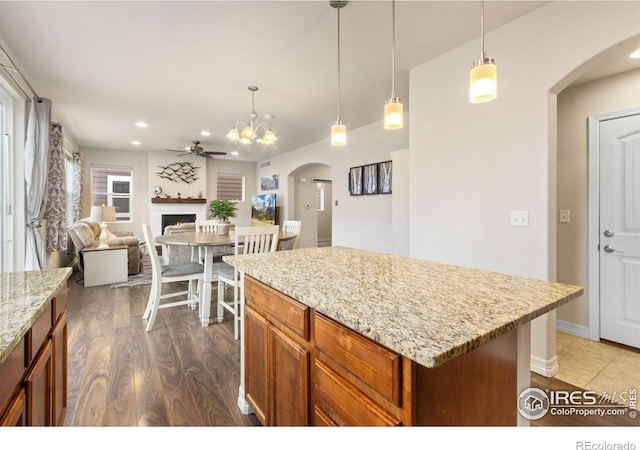 kitchen with open floor plan, ceiling fan with notable chandelier, arched walkways, pendant lighting, and brown cabinetry