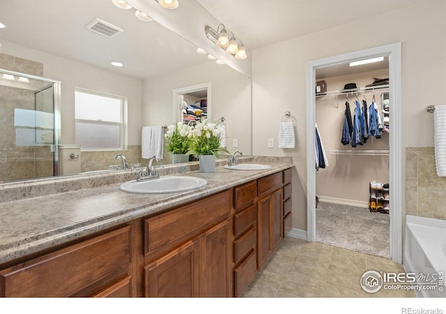 full bath with a shower stall, a sink, a walk in closet, and visible vents