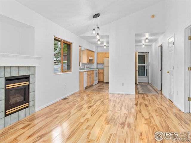 1010 S Saint Vrain Ave S, Estes Park, CO 80517 - unfurnished living room featuring light wood finished floors, a tiled fireplace, vaulted ceiling, baseboards, and a sink