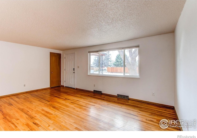 spare room featuring a textured ceiling, visible vents, baseboards, and wood-type flooring