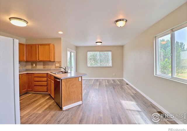 kitchen featuring a peninsula, light countertops, freestanding refrigerator, stainless steel dishwasher, and a sink