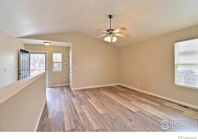 spare room with lofted ceiling, light wood-style floors, baseboards, and ceiling fan