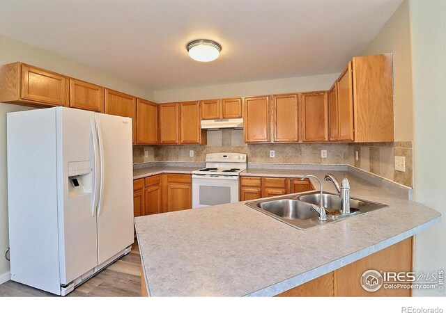 kitchen featuring tasteful backsplash, white appliances, a peninsula, under cabinet range hood, and a sink