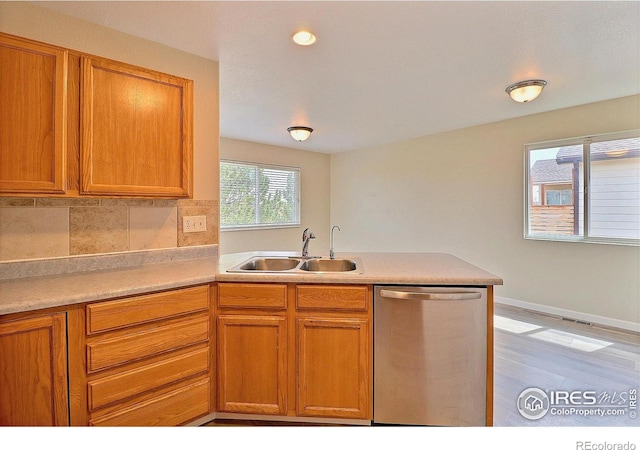 kitchen featuring a peninsula, light countertops, backsplash, dishwasher, and a sink