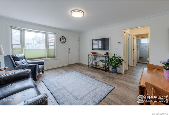 living room featuring baseboards, light wood-style flooring, and crown molding