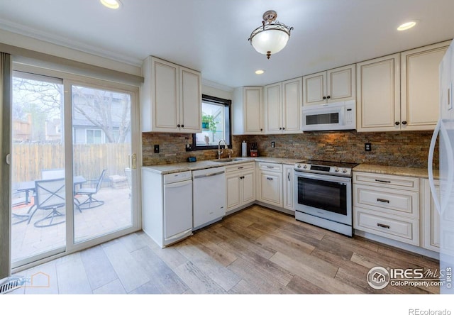 kitchen featuring crown molding, a sink, white appliances, light wood-style floors, and decorative backsplash