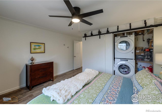 bedroom featuring stacked washer / dryer, baseboards, ornamental molding, ceiling fan, and wood finished floors