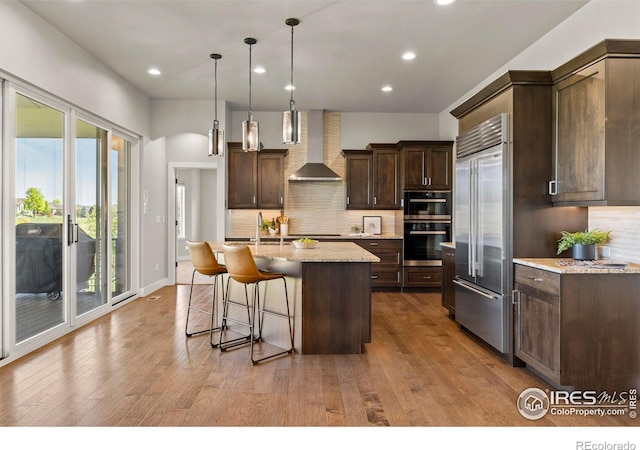 5977 Crooked Stick Dr, Windsor, CO 80550 - kitchen with wall chimney range hood, stainless steel built in fridge, dark brown cabinets, recessed lighting, and tasteful backsplash