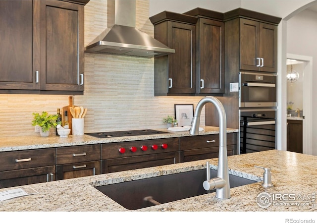 5977 Crooked Stick Dr, Windsor, CO 80550 - kitchen with wall chimney range hood, dark brown cabinets, black electric cooktop, and light stone countertops