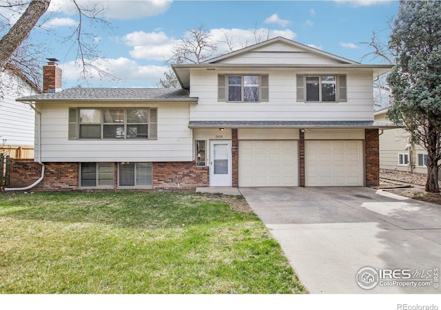split level home featuring an attached garage, a chimney, concrete driveway, a front yard, and brick siding