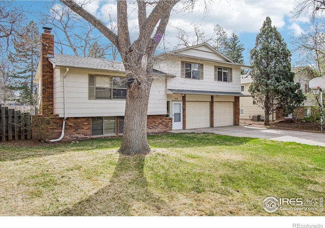tri-level home with concrete driveway, a chimney, an attached garage, fence, and a front lawn