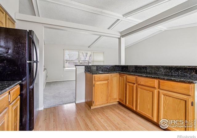 kitchen featuring dark stone countertops, baseboards, light wood finished floors, freestanding refrigerator, and vaulted ceiling with beams