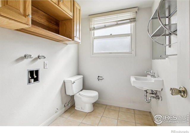 half bathroom featuring a sink, baseboards, toilet, and tile patterned flooring