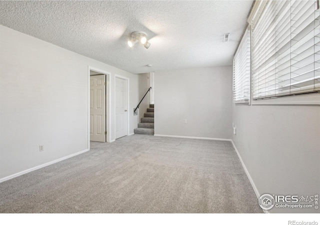 carpeted empty room featuring baseboards, a textured ceiling, and stairway
