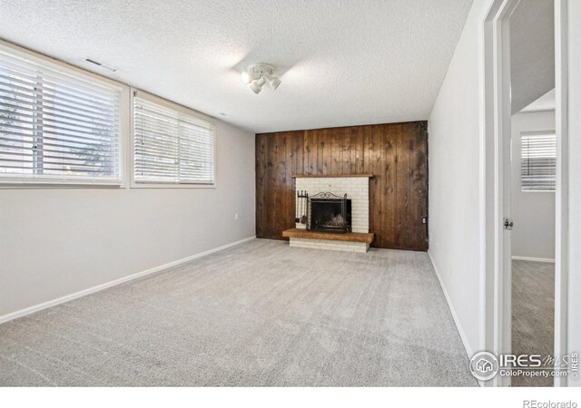 unfurnished living room with wood walls, baseboards, a textured ceiling, carpet floors, and a brick fireplace