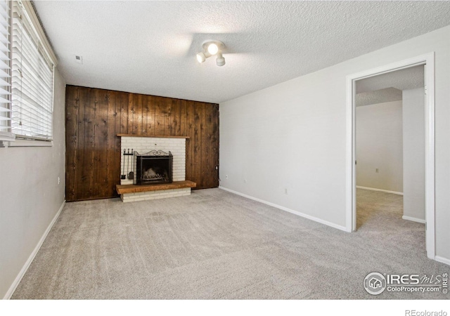 unfurnished living room with carpet flooring, a textured ceiling, wood walls, a brick fireplace, and baseboards