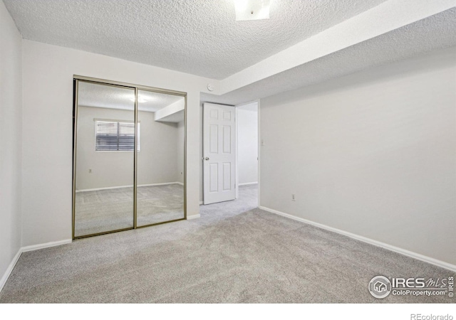 unfurnished bedroom with carpet, a closet, a textured ceiling, and baseboards