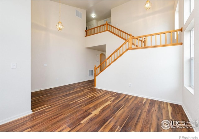 unfurnished living room featuring visible vents, wood finished floors, a towering ceiling, and stairway