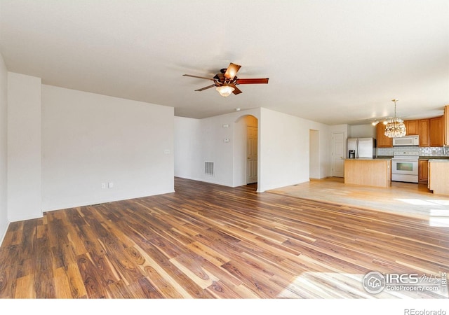 unfurnished living room with ceiling fan with notable chandelier, visible vents, arched walkways, and light wood-type flooring