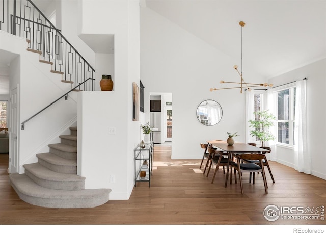 dining room with wood finished floors, high vaulted ceiling, stairway, and an inviting chandelier