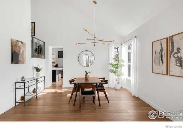 dining space with hardwood / wood-style flooring, baseboards, a chandelier, and high vaulted ceiling