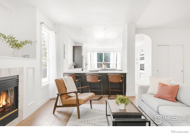 living room with recessed lighting, arched walkways, light wood-type flooring, baseboards, and a tiled fireplace